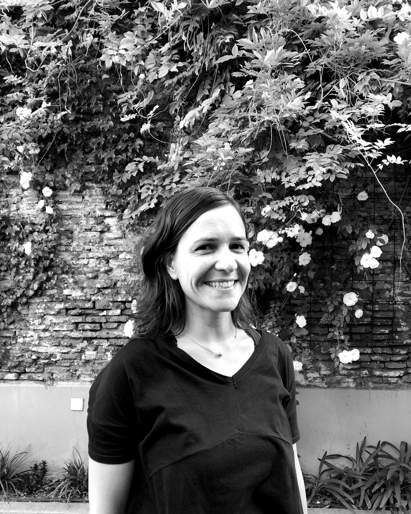 Ine sonriendo frente a una pared de ladrillos con plantas